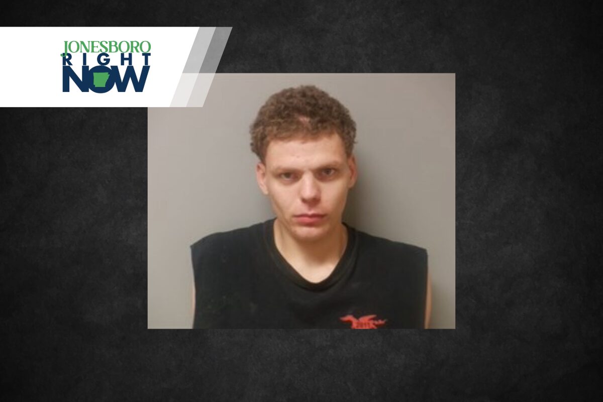 Mugshot of a young man with short curly hair in a black sleeveless shirt against a gray wall, with a Jonesboro Right Now logo in the top-left corner.
