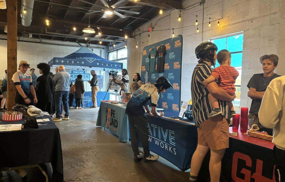 Indoor community event with multiple info booths, string lights, and people browsing tables along the room.