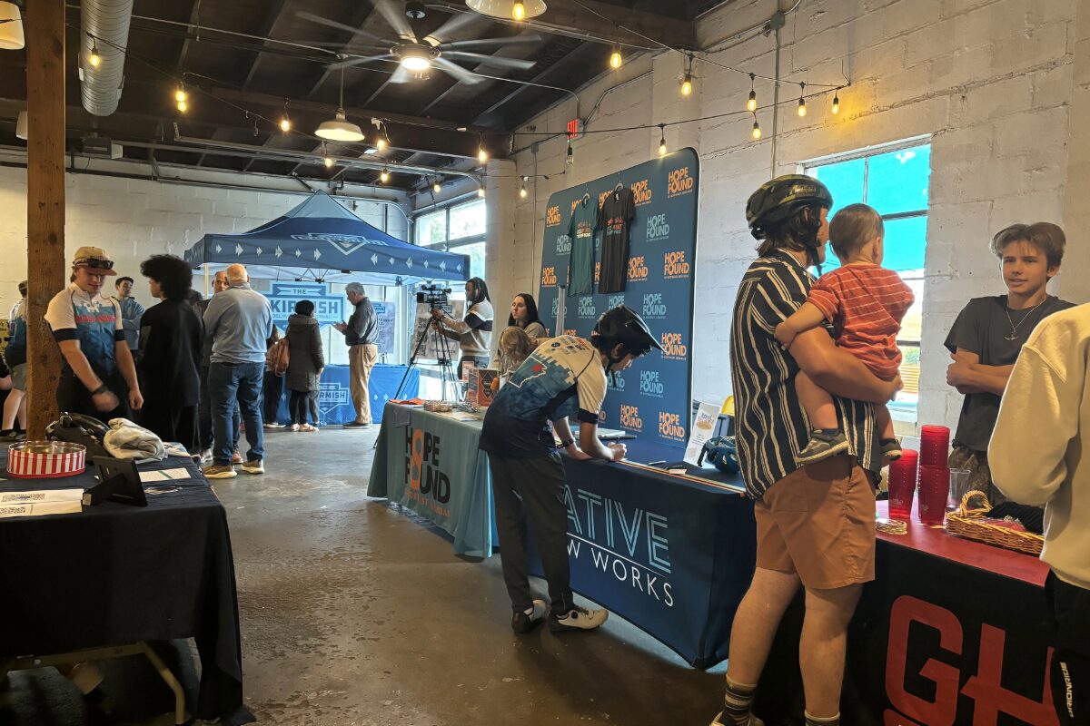 Indoor community event with multiple info booths, string lights, and people browsing tables along the room.