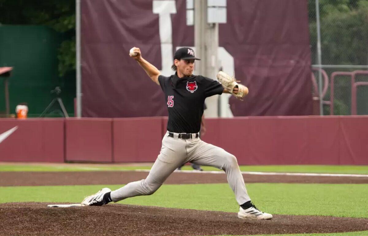 Baseball pitcher in black uniform throwing a pitch from the mound, left leg extended forward and body in motion.