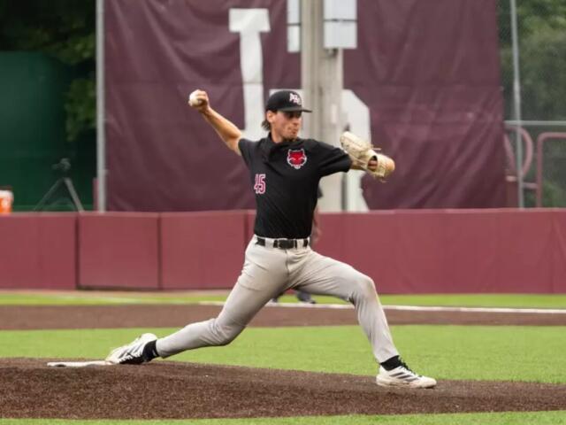 Baseball pitcher in black uniform throwing a pitch from the mound, left leg extended forward and body in motion.