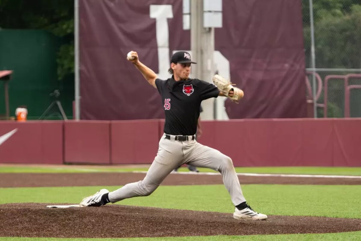 Baseball pitcher in black uniform throwing a pitch from the mound, left leg extended forward and body in motion.