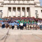 Large diverse group posing on the steps of a grand neoclassical building with tall columns.