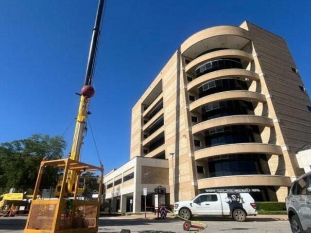 Construction crane beside a tall curved beige office building, with work vans parked in front.