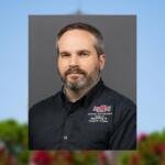 Portrait of a man with short hair and a gray beard, wearing a black Arkansas State University Engineering & Computer Science shirt against a gray backdrop.