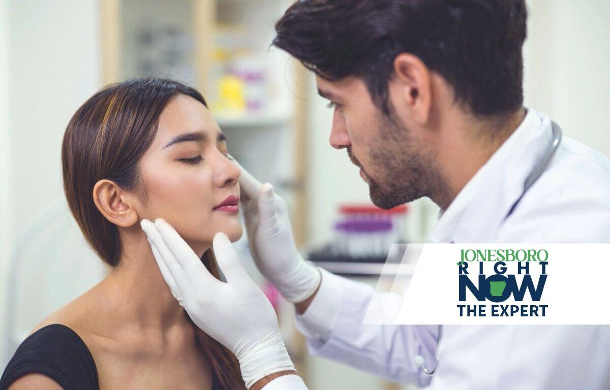 Medical professional wearing gloves examines a woman's face in a clinical setting.