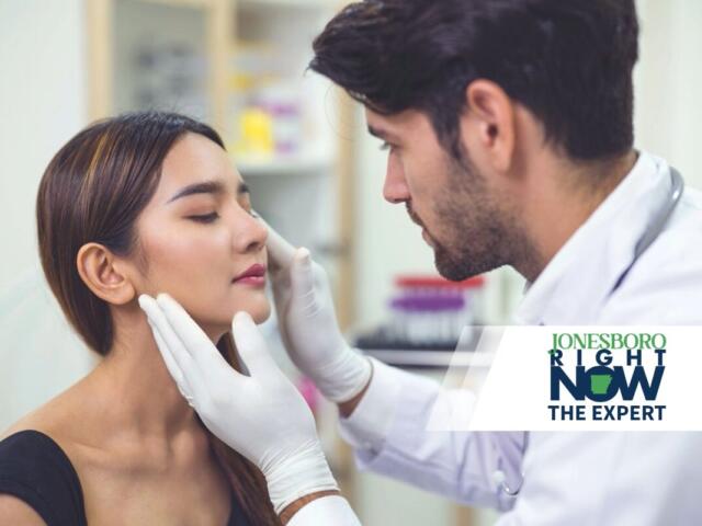 Medical professional wearing gloves examines a woman's face in a clinical setting.