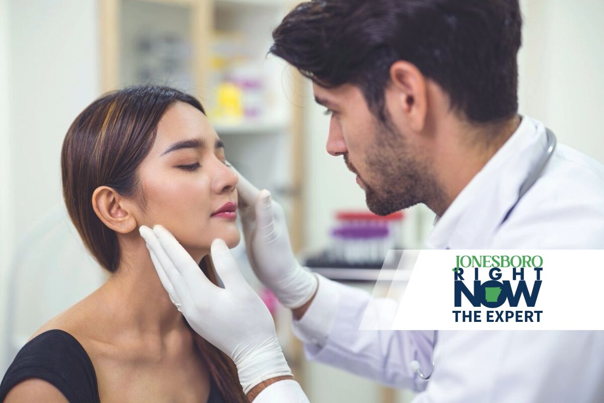 Medical professional wearing gloves examines a woman's face in a clinical setting.