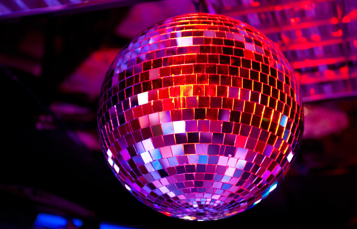 Disco ball hanging in a dark club, its mirrored tiles reflecting purple and pink lights.