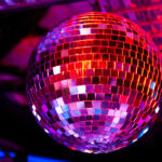 Disco ball hanging in a dark club, its mirrored tiles reflecting purple and pink lights.