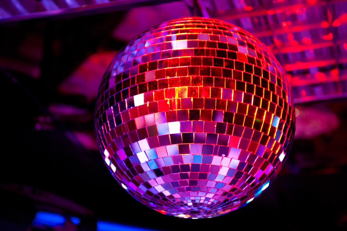 Disco ball hanging in a dark club, its mirrored tiles reflecting purple and pink lights.
