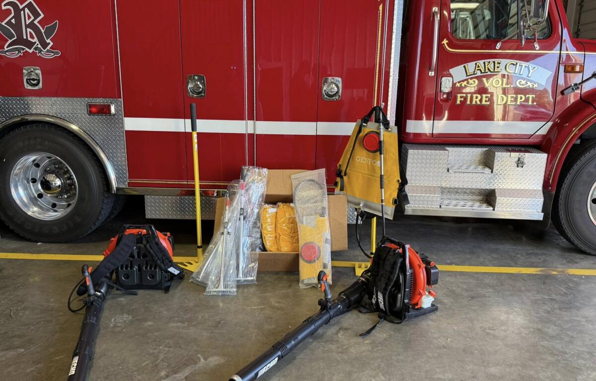 Red Lake City fire truck side with equipment on the floor in front, hoses, and tool bags scattered nearby inside a fire station bay.
