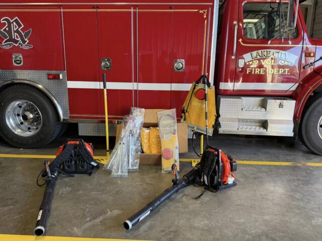Red Lake City fire truck side with equipment on the floor in front, hoses, and tool bags scattered nearby inside a fire station bay.