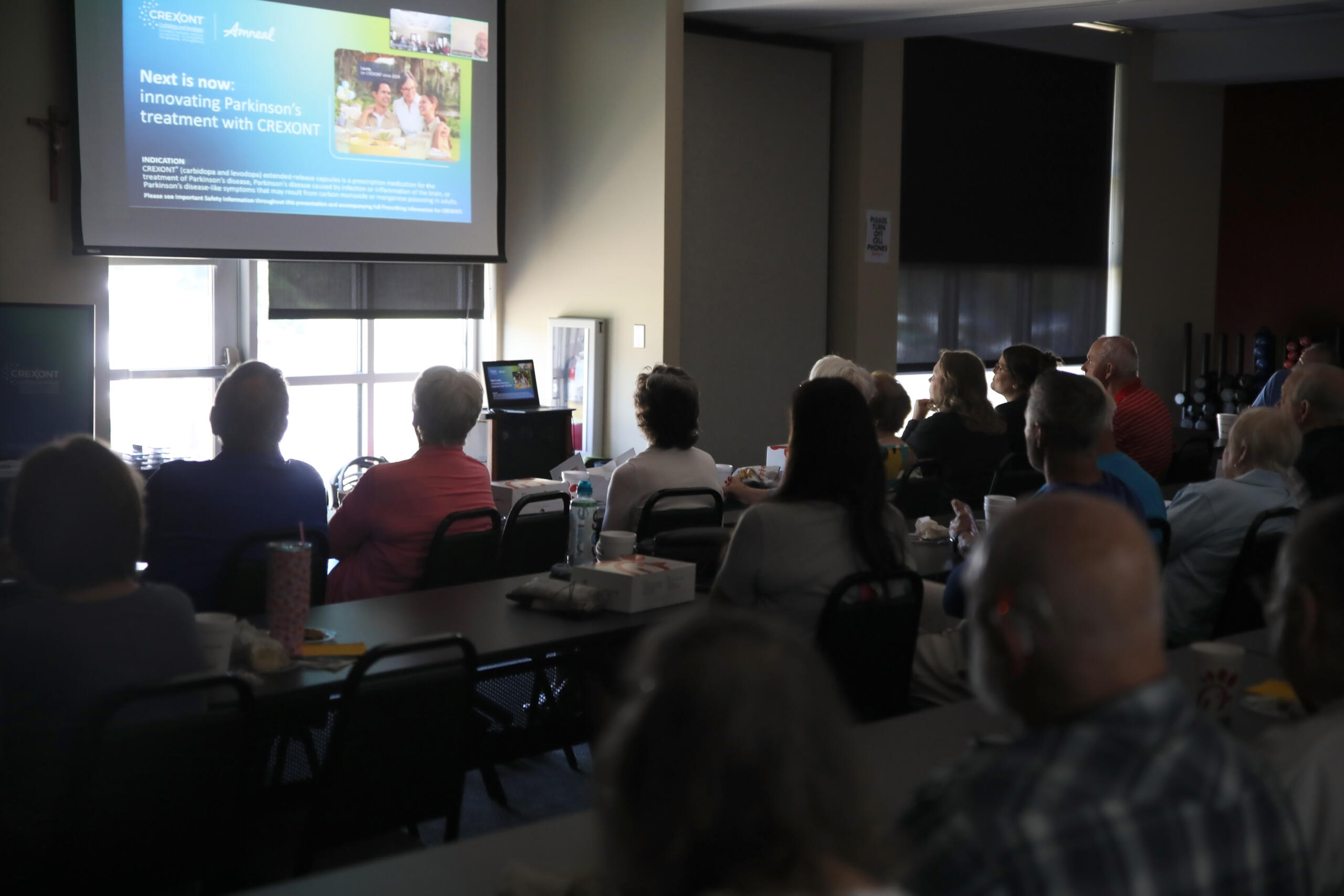 Audience seated in a conference room watching a projector screen displaying a presentation at the front of the room.