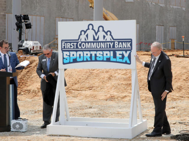Three men in suits at a groundbreaking ceremony beside a 'First Community Bank Sportsplex' sign on a construction site.