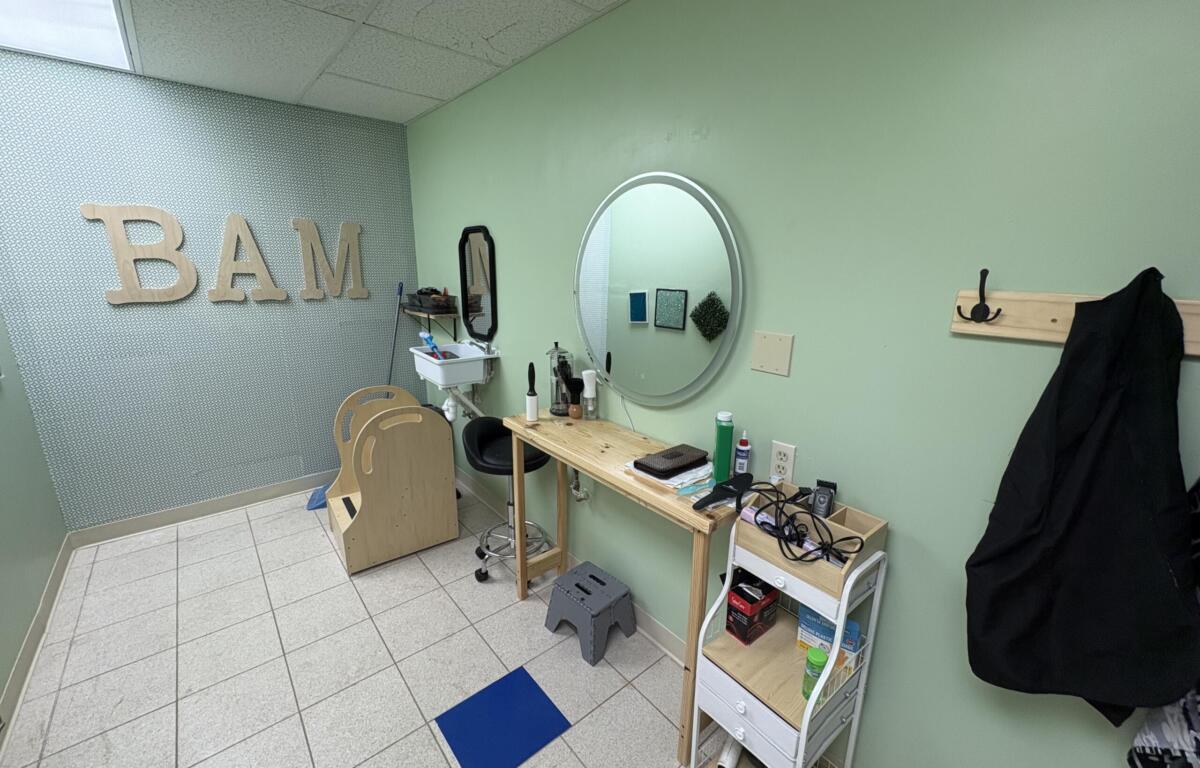 Salon styling station with round mirror, wooden worktable, and hair tools against mint-green walls; large wooden BAM letters on patterned wall.