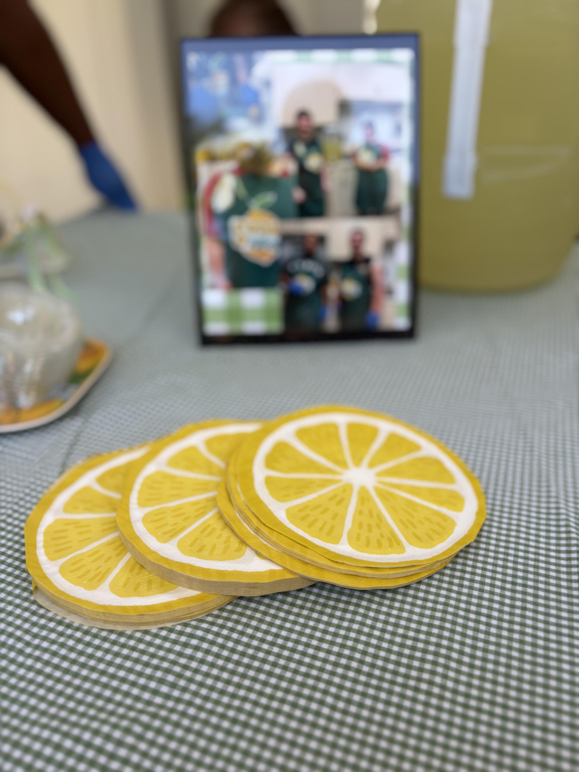 Stack of yellow lemon-slice coasters on a green-and-white checkered tablecloth, with a blurred photo frame in the background.