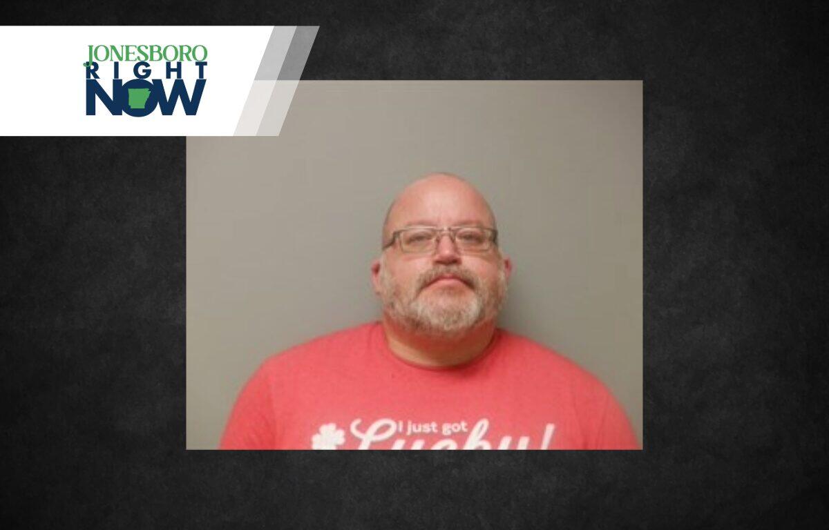 Mugshot-style portrait of a bald man with glasses and gray beard wearing a pink T‑shirt against a gray background; Jonesboro Right Now banner in the corner.