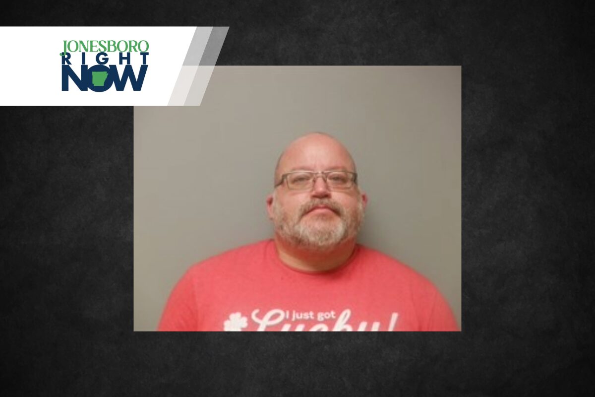 Mugshot-style portrait of a bald man with glasses and gray beard wearing a pink T‑shirt against a gray background; Jonesboro Right Now banner in the corner.