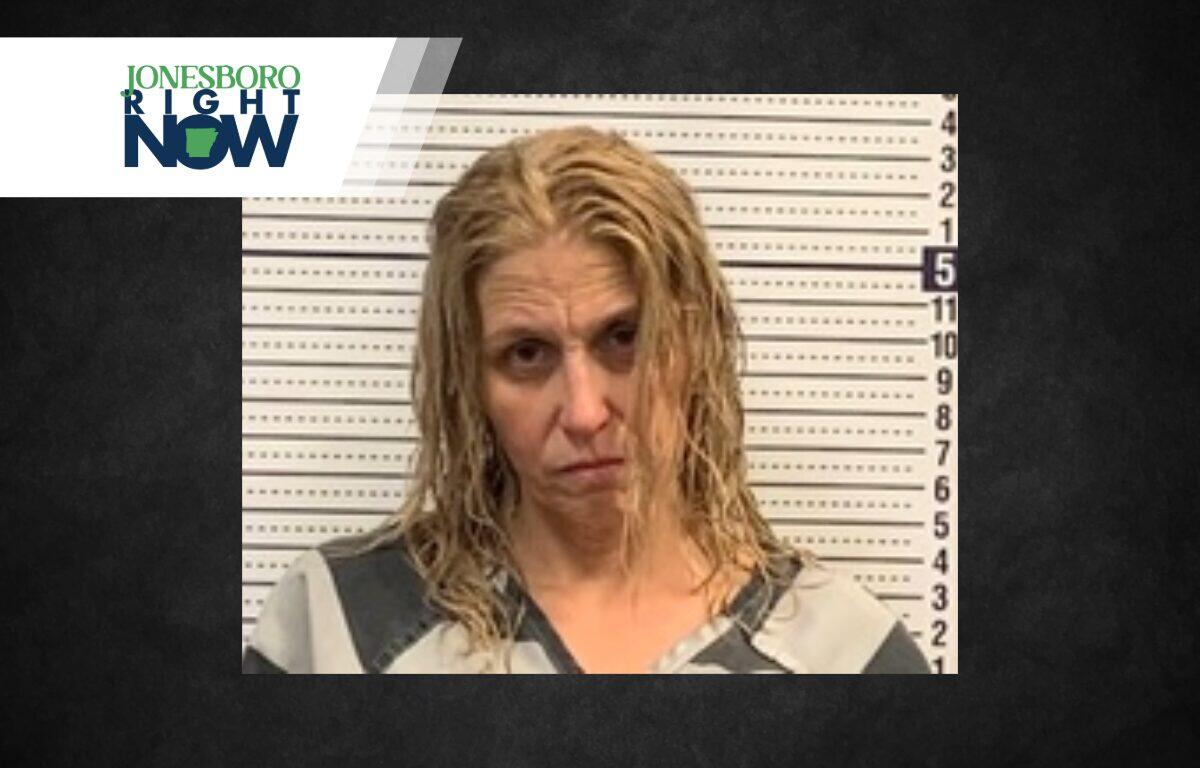 Mugshot of a woman with wet blond hair in a gray and black striped jumpsuit, standing against a height chart; Jonesboro Right Now logo in corner.