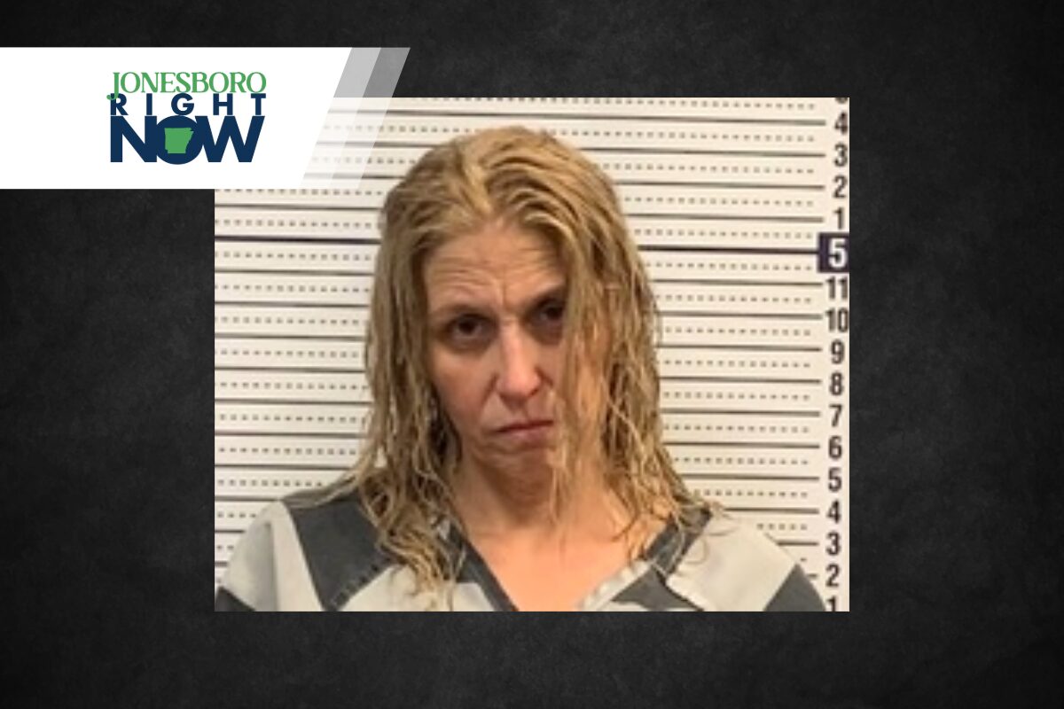 Mugshot of a woman with wet blond hair in a gray and black striped jumpsuit, standing against a height chart; Jonesboro Right Now logo in corner.