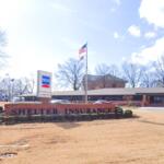 Shelter Insurance office with a brick sign in front reading 'Shelter Insurance' and an American flag nearby; a white van is parked to the right.