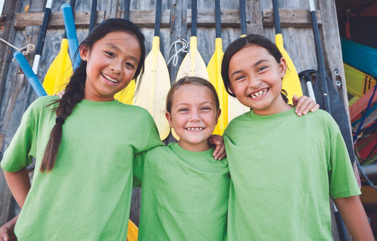 three girls in green shirts in front of yellow canoe paddles