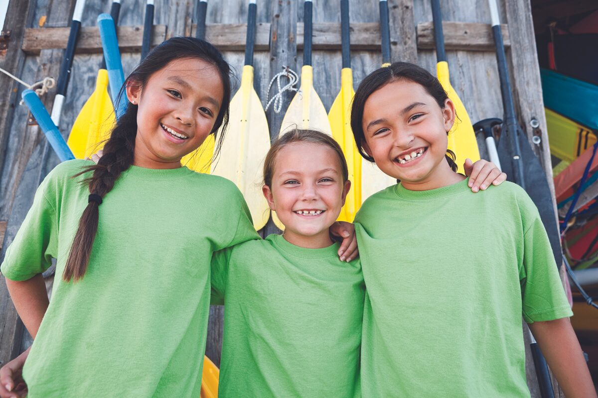 three girls in green shirts in front of yellow canoe paddles