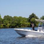 White state water patrol boat speeding on a calm lake, two officers on board with shoreline trees in the background.