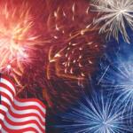 American flag waves in the foreground with red, white, and blue fireworks bursting in the night sky.