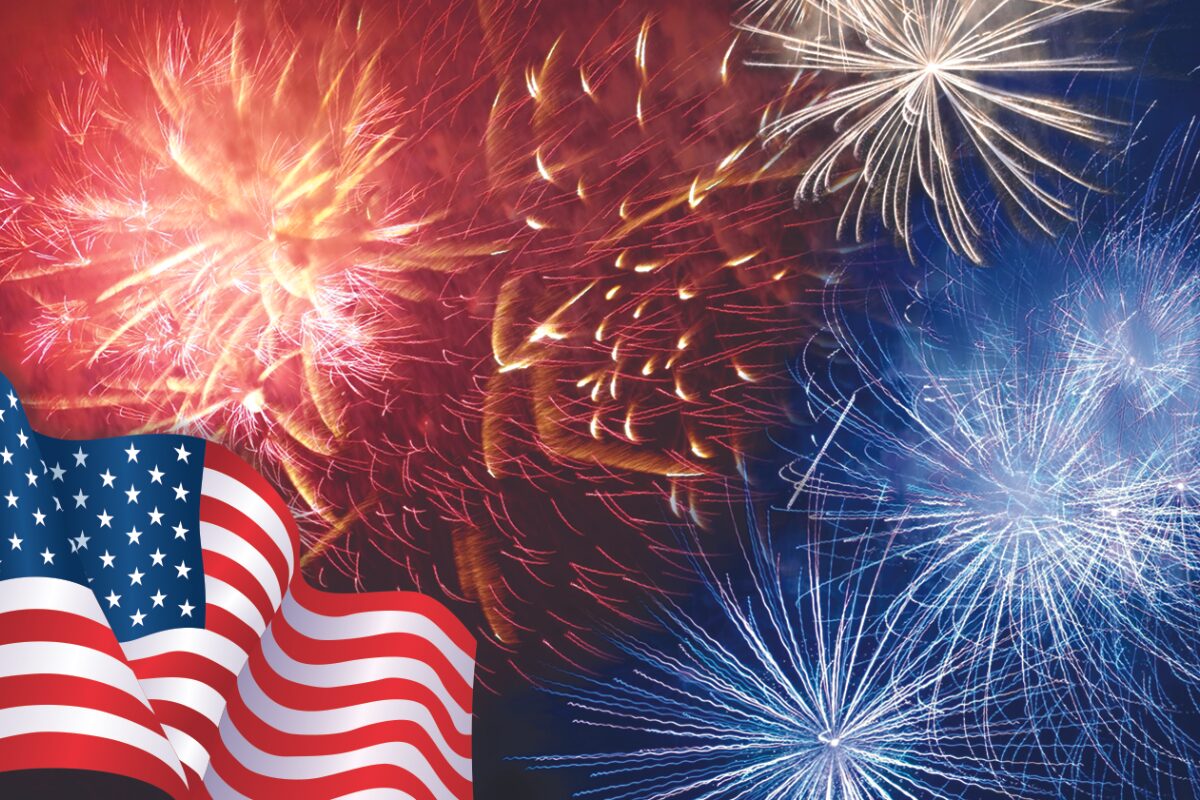 American flag waves in the foreground with red, white, and blue fireworks bursting in the night sky.
