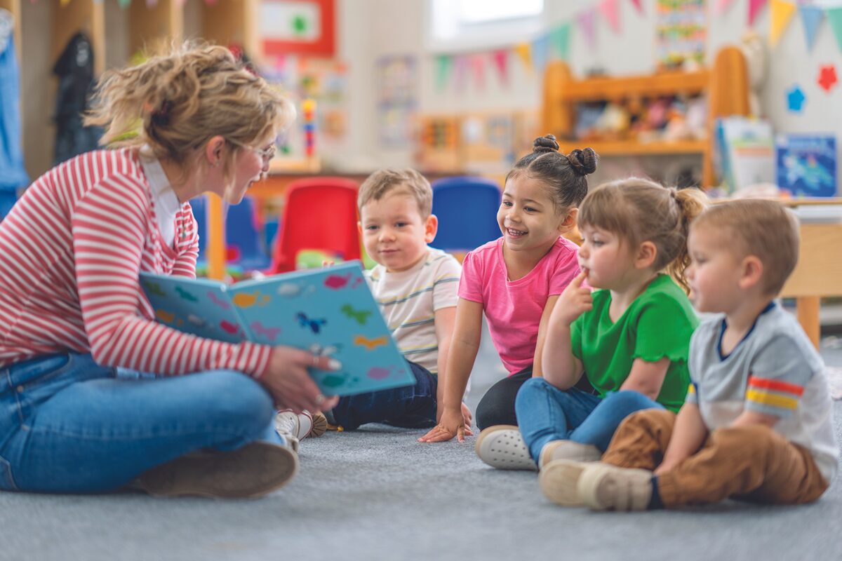 woman holding book and showing it to a group of young children