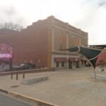 Brick building with storefronts and a large 'The Forum' sign, plus a digital marquee in front and a concrete plaza area.