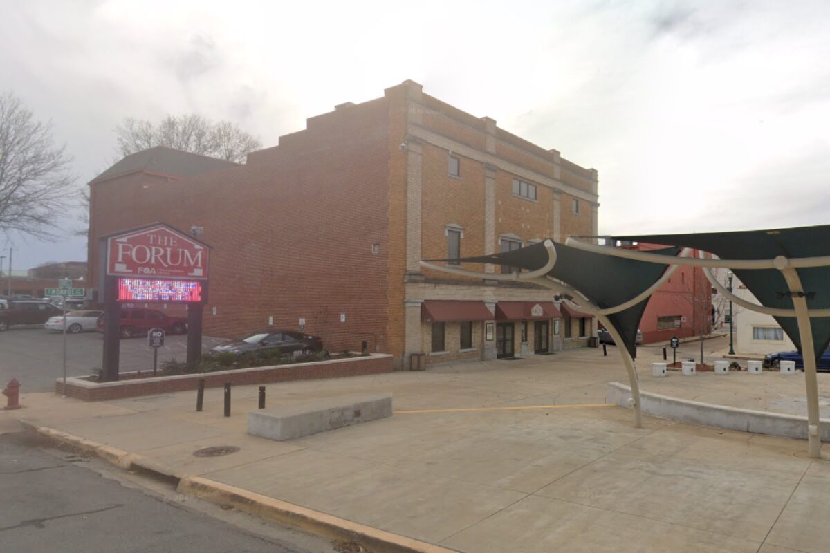 Brick building with storefronts and a large 'The Forum' sign, plus a digital marquee in front and a concrete plaza area.