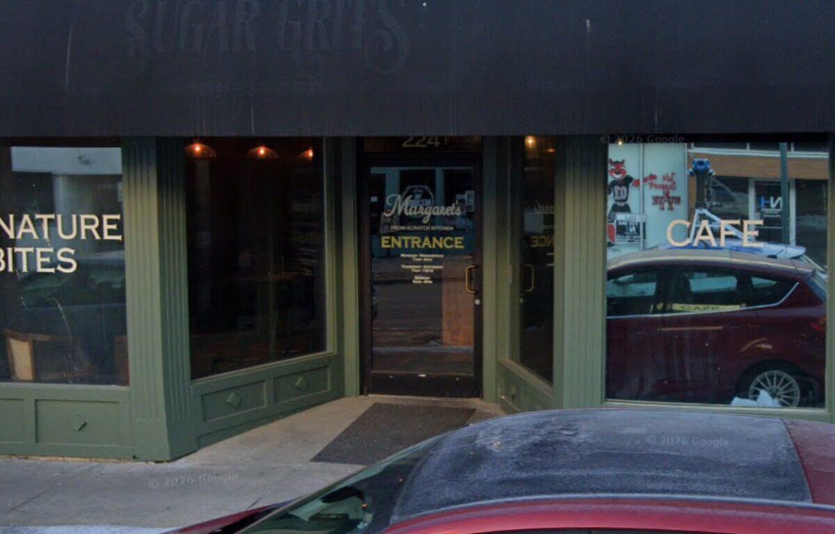 Green storefront with glass windows; left sign reads 'NATURE BITES', right sign 'CAFE', door in center labeled 'ENTRANCE' with a car parked outside.