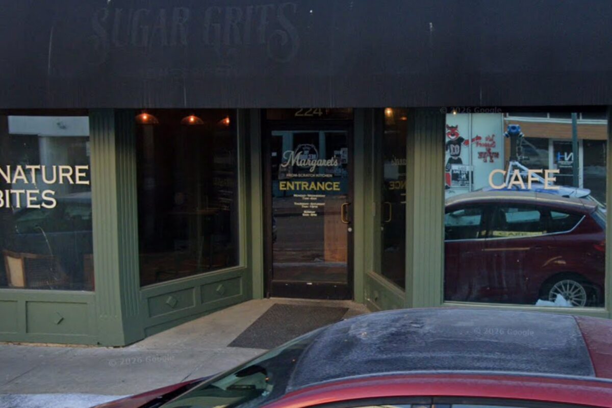 Green storefront with glass windows; left sign reads 'NATURE BITES', right sign 'CAFE', door in center labeled 'ENTRANCE' with a car parked outside.