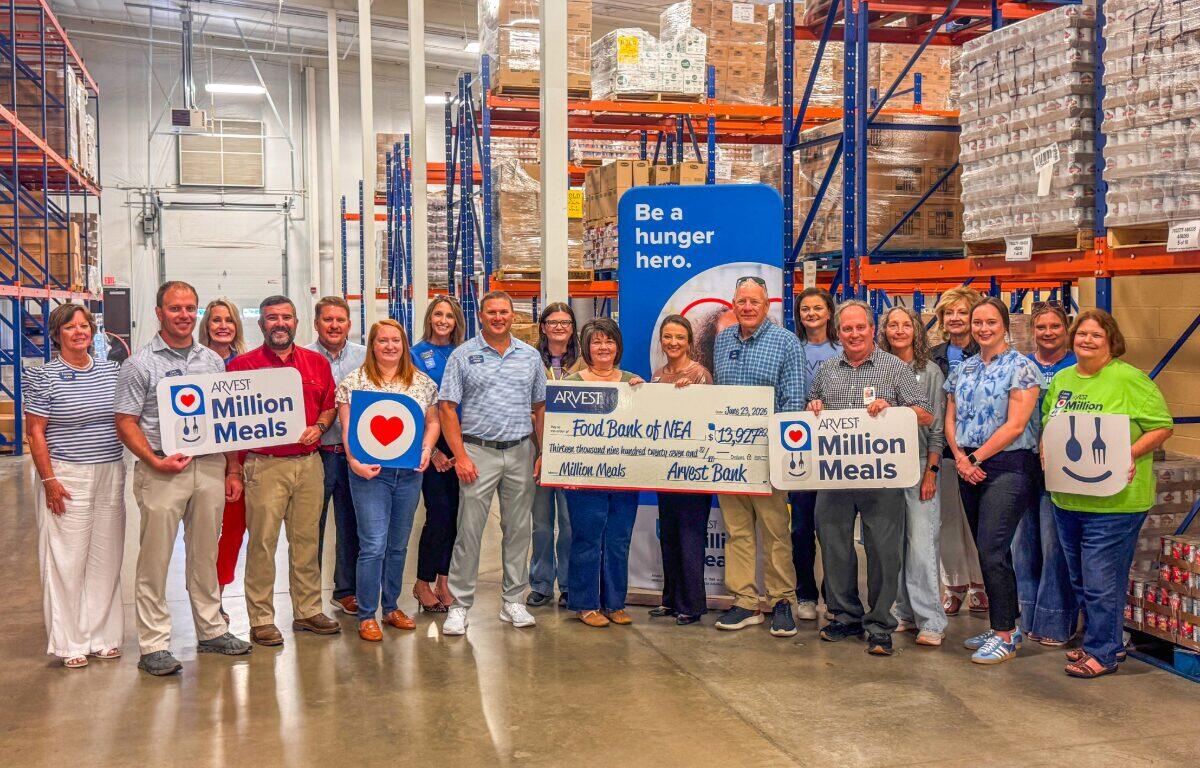 Group of people in a warehouse holding 'Million Meals' signs and a large donation check, highlighting a hunger relief event.