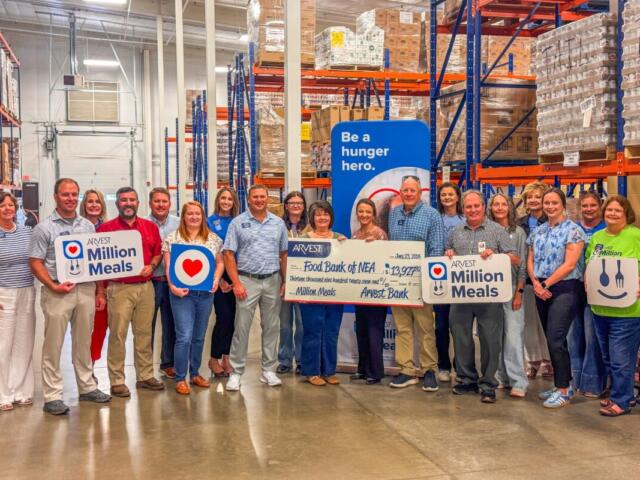Group of people in a warehouse holding 'Million Meals' signs and a large donation check, highlighting a hunger relief event.