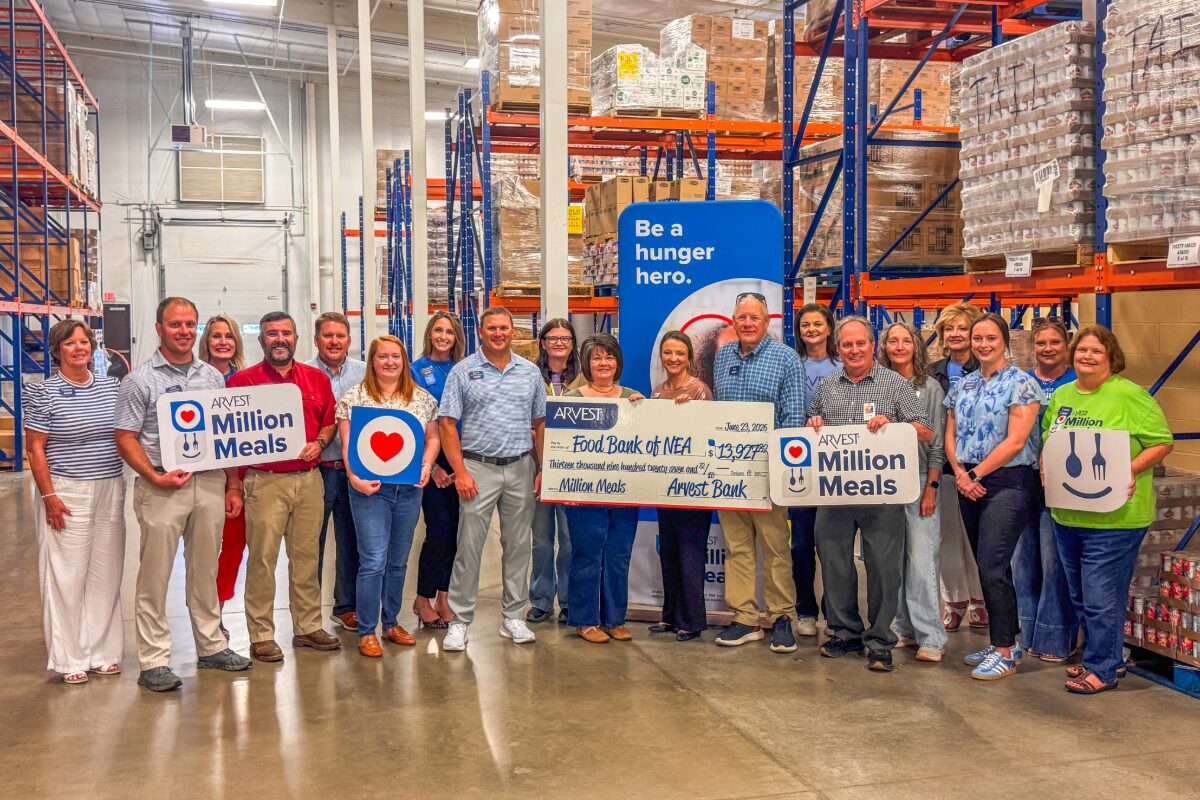Group of people in a warehouse holding 'Million Meals' signs and a large donation check, highlighting a hunger relief event.