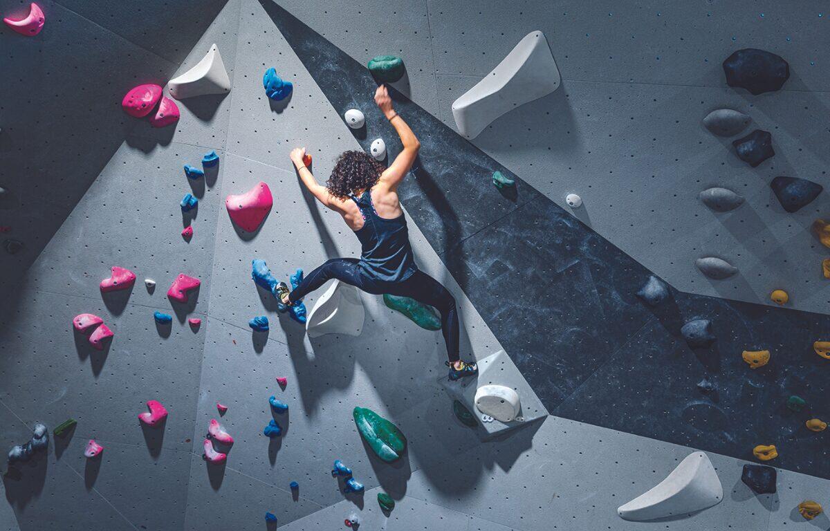 woman with curly hair climbs in bouldering gym