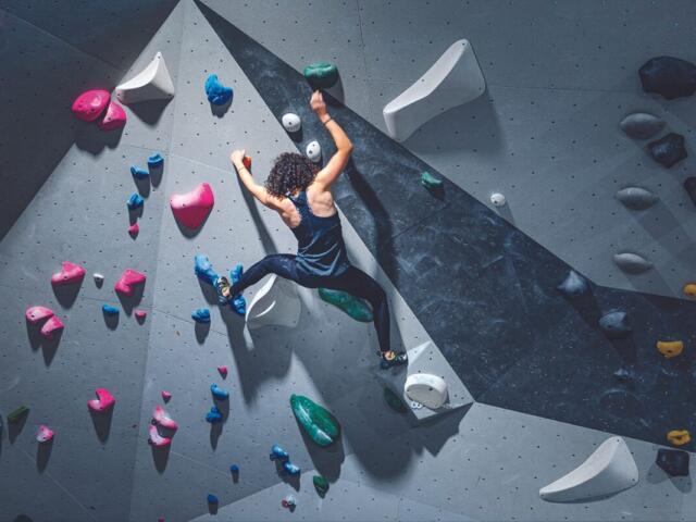 woman with curly hair climbs in bouldering gym