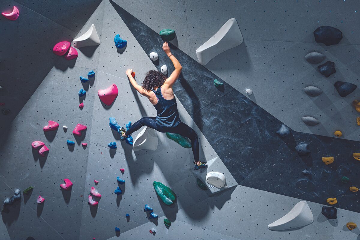 woman with curly hair climbs in bouldering gym