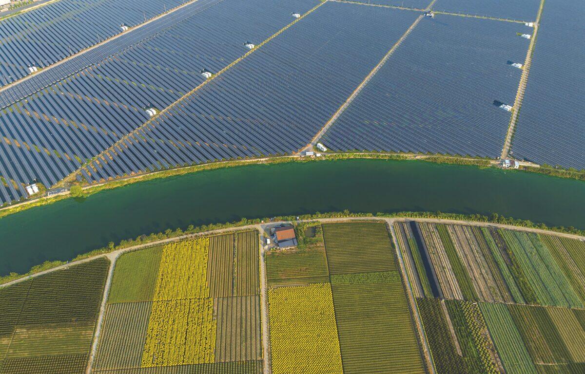 Aerial view of a large solar farm separated from colorful patchwork fields by a winding canal.