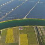 Aerial view of a large solar farm separated from colorful patchwork fields by a winding canal.