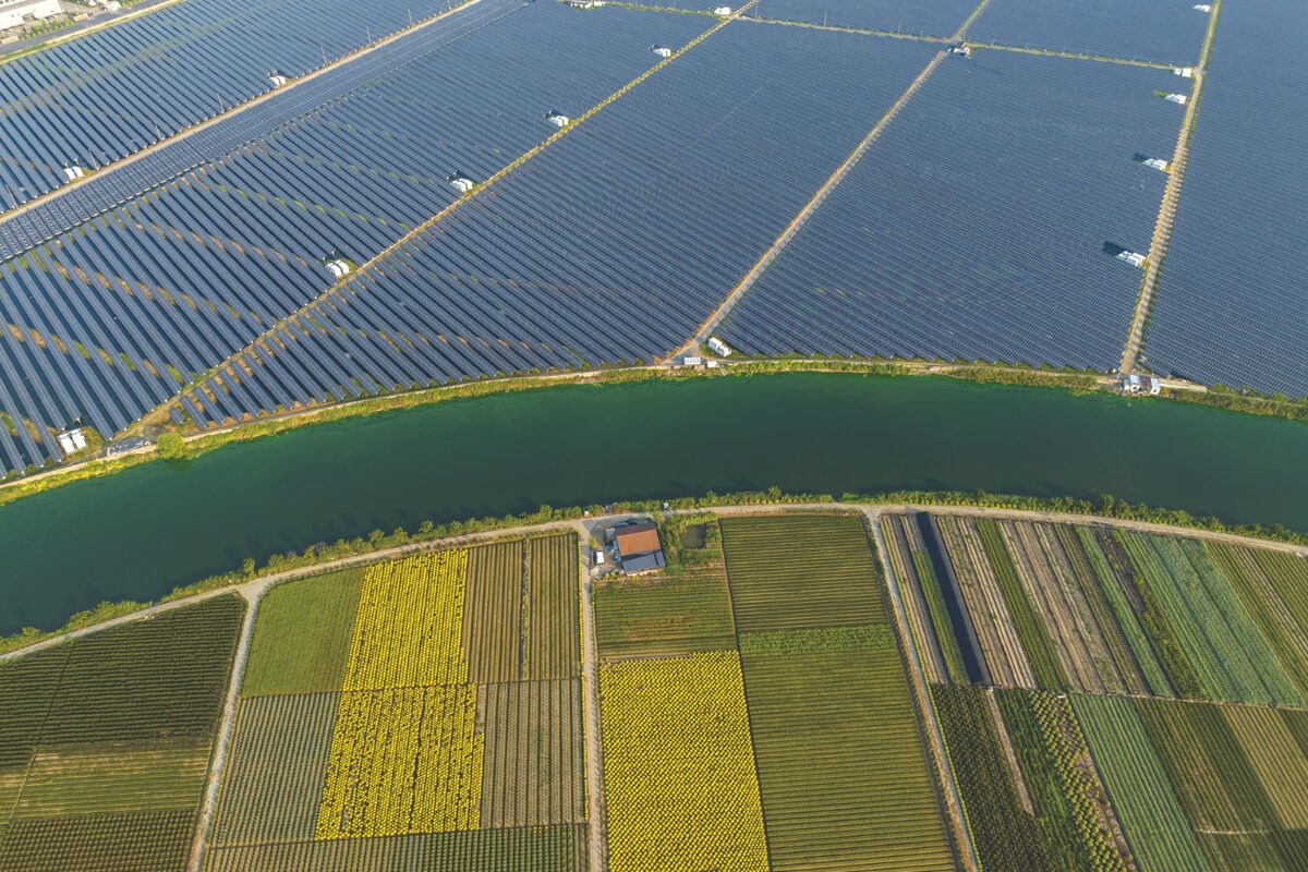 Aerial view of a large solar farm separated from colorful patchwork fields by a winding canal.