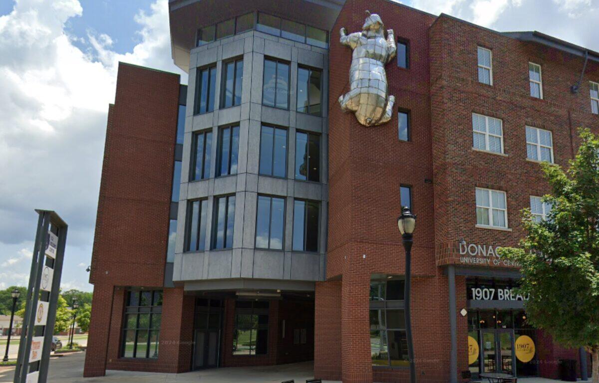 Brick university building with a large silver metal sculpture of a figure mounted on the wall.