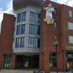 Brick university building with a large silver metal sculpture of a figure mounted on the wall.