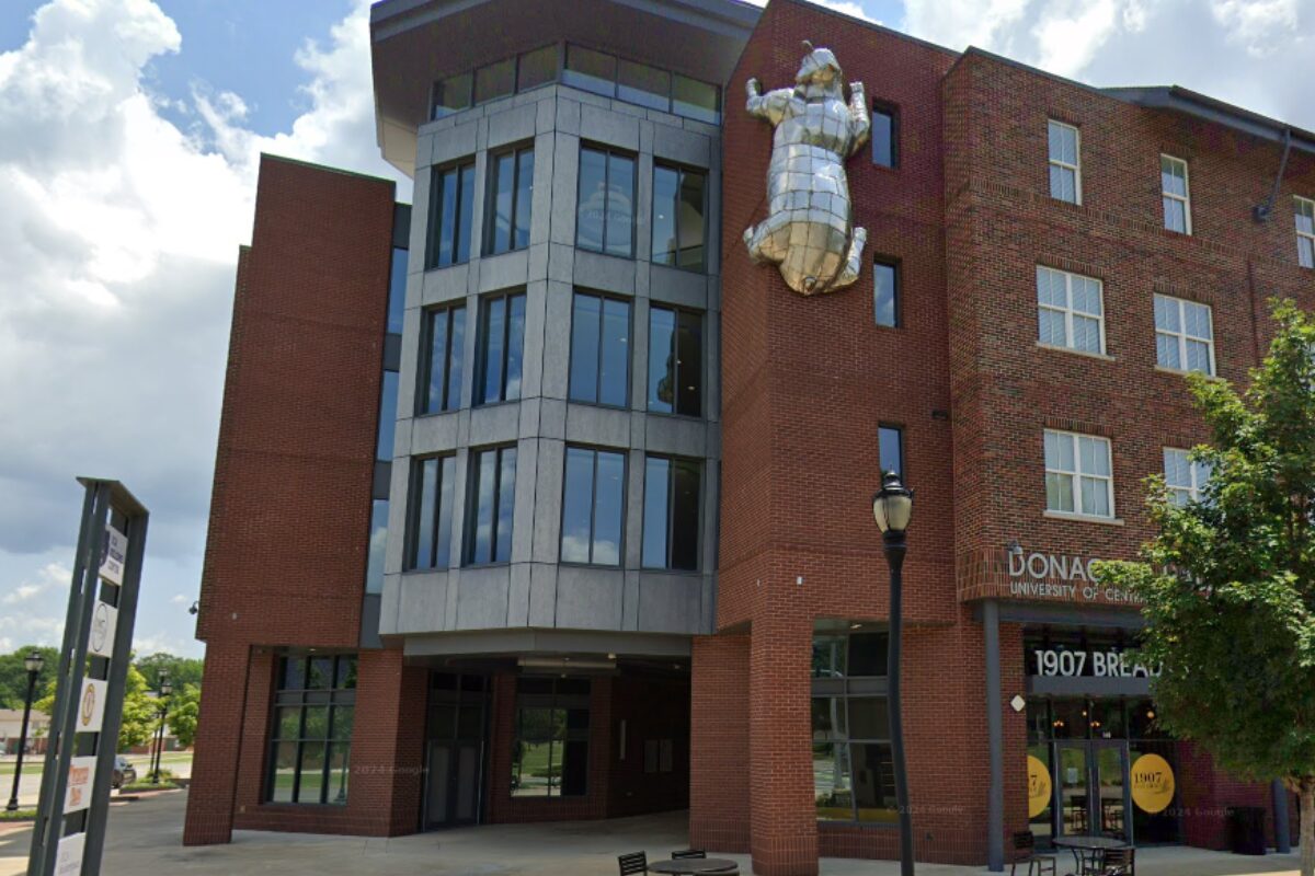 Brick university building with a large silver metal sculpture of a figure mounted on the wall.