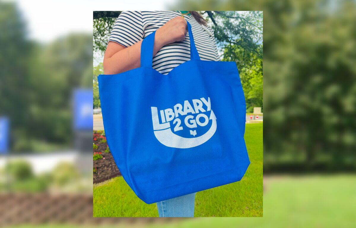 Blue tote bag with 'Library 2 Go' logo being carried outdoors. I