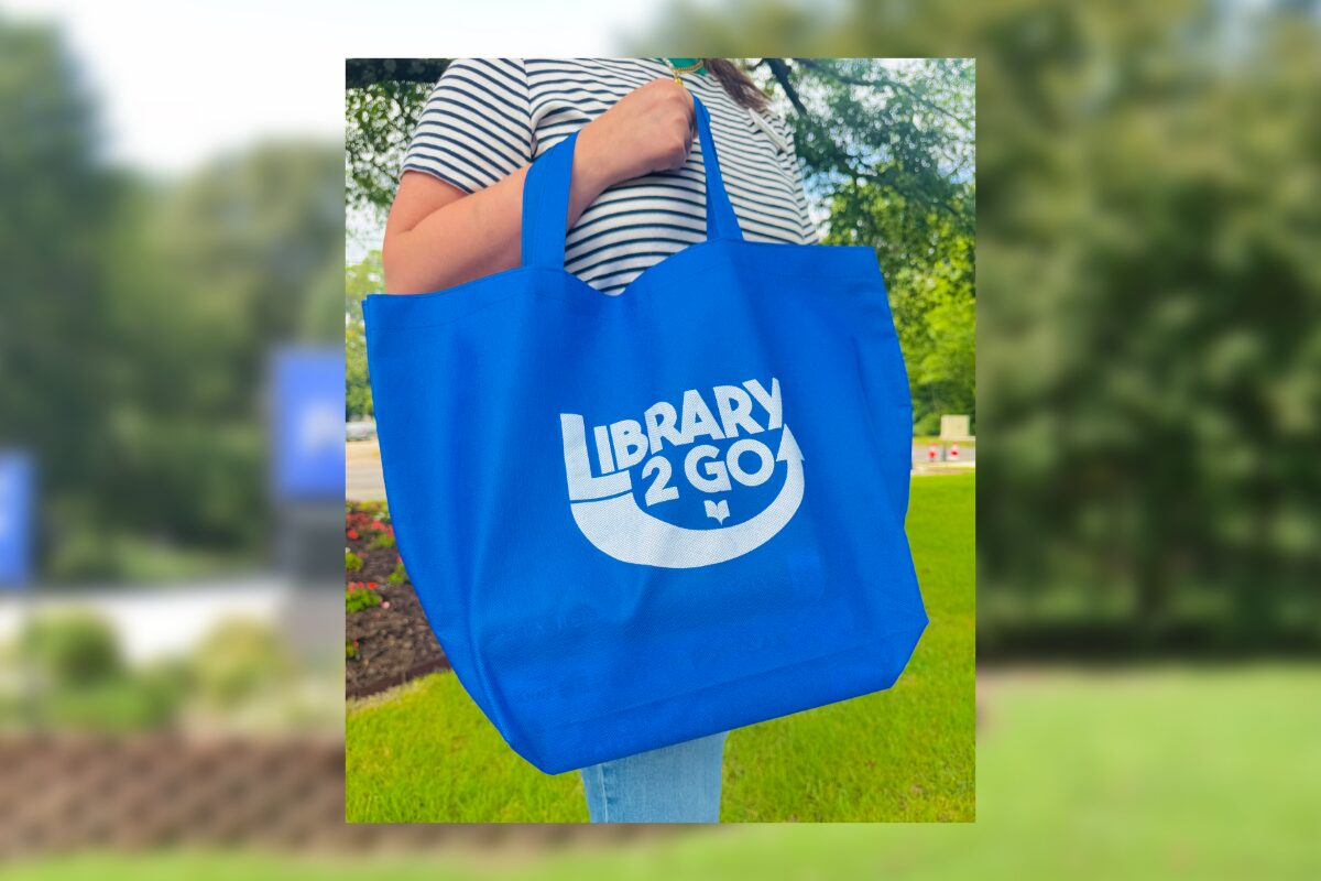 Blue tote bag with 'Library 2 Go' logo being carried outdoors. I